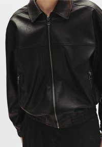Czarna kurtka z sztucznej skóry z kołnierzykiem, zamek z przodu, kieszenie boczne i elastyczny dół. Gładka faktura, lekko luźny krój.