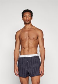 Tums zilāsvītra apakšveļa ar baltu jostu, uz kuras redzams "Calvin Klein" logo. Priekšējā daļa ar pogu aizdari, izgatavota no kokvilnas materiāla ar mīkstu tekstūru.