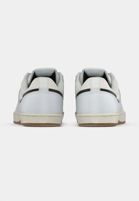 Λευκά αθλητικά παπούτσια με λεία δερμάτινη επιφάνεια, διαθέτοντας γκρι λωρίδα ως ακοή, επενδεδυμένο κολάρο και σόλα από καουτσούκ γκόμ. Απλός σχεδιασμός, χωρίς λογότυπα.