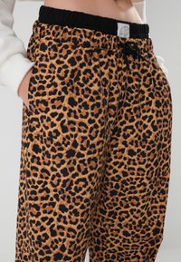 Joggerice sa leopard uzorkom, elastičnim crnim pojasom, detaljem vezanja i bočnim džepovima. Teksturirana tkanina u toplim smeškastim i crnim bojama.
