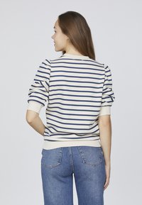 Creme sweatshirt med marineblå striber, puffede ærmer og ribbede manchetter. Sammen med højtsiddende blå jeans. Bagview, der viser designdetaljer.