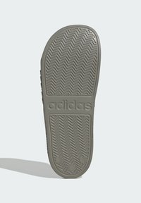 Suola delle calzature Adidas in gomma grigia scura con un motivo a zig zag, caratterizzata dal marchio in rilievo. Design piatto con una leggera curvatura.