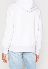 Sudadera con capucha lila de ajuste holgado, con puños y dobladillo de canalé, que incluye capucha y detalles de costuras mínimas. Combinada con mezclilla de lavado claro.