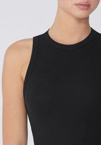 Schwarzes geripptes Tanktop mit rundem Ausschnitt und ärmellosem Design, das eine glatte Textur und eine figurbetonte Silhouette zeigt.