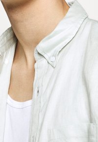 Ljusgrön, skjorta med krage, tillverkad av ett strukturerat tyg, med en delvis knäppt knappslå och en enda bröstficka.