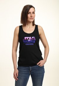 Černý tílko s potiskem "STAR WARS MANDALORIAN" v purpurové a růžové barvě. Materiál je hladký, s širokými ramínky a volným střihem.