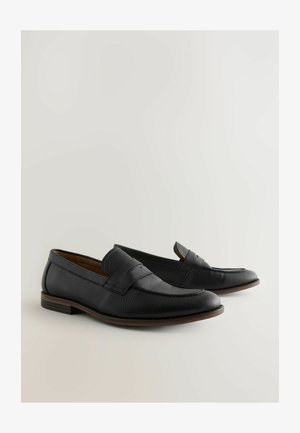 Mocassins en cuir noir avec une finition texturée, un bout rond et une sangle décorative sur le dessus, avec un petit talon.