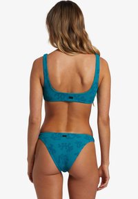 Teal bikini-set med ribbad textur. Toppen har breda axelband och en fyrkantig rygg, medan byxorna är lågt skurna med ett subtilt mönster.