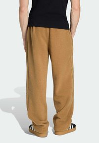 Braune Fleece-Sweathosen mit lockerem Schnitt, mit Seitennähten und einer weichen Textur, kombiniert mit schwarzen Sandalen.