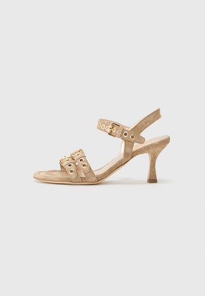 Beige Wildleder-Absatzsandale mit drei Riemen und goldenen Hardware-Akzenten. Offene Zehenpartie und ein schlanker, geschwungener Absatz.
