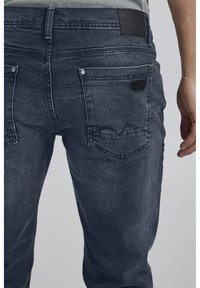 Jeans i mörk marinblått med en urviven textur. Har två bakfickor och en liten läderetikett nära midjan.