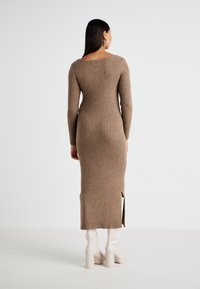 Robe midi en tricot marron avec texture côtelée, manches longues et fente au dos. Associée à des bottes à talons bloc crème montant jusqu'à la cheville.