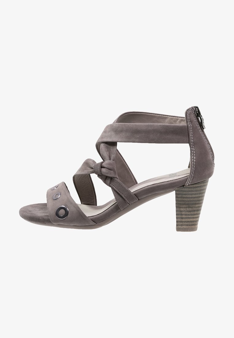 Sandale à talons hauts en suède gris avec des lanières nouées, des accents circulaires sur les orteils et un talon carré texturé. Bride de cheville ajustable incluse.