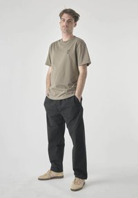 Khaki cotton t-shirt with short sleeves and a small logo, paired with black pants and beige sneakers featuring pink stripes.