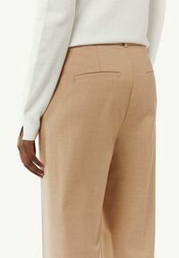 Pantaloni beige sartoriali con una texture liscia, dotati di una vita piatta, tasche laterali e due tasche posteriori.