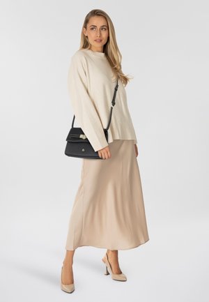 Beiger Strickpullover, fließender Midirock in hellem Beige, schwarze Handtasche mit Verschluss und nudefarbene High Heels. Glatte Texturen überall.