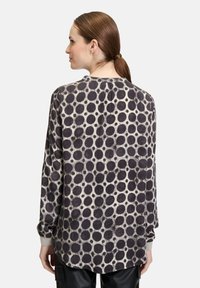 Long-sleeve shirt featuring a beige background with large black polka dots, relaxed fit, and ribbed cuffs. Back view displayed.