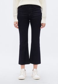 Σκούρο μπλε τζιν παντελόνι καμπάνα με ψηλή μέση, με λεία υφή και εμφανείς ραφές, συνδυασμένο με λευκά αθλητικά παπούτσια.