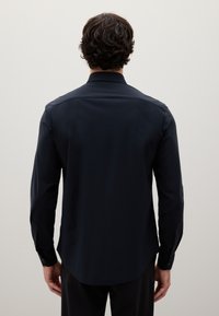 Camicia blu navy con collo classico, maniche lunghe e orlo curvo. Texture liscia con dettaglio sulla spalla posteriore e bottoni ai polsi.