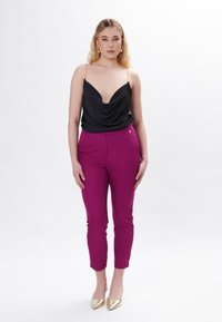 Camisón de satén negro con escote drapeado, combinado con pantalones ajustados rosa brillante. La modelo lleva tacones de punta dorada. Diseño simple y elegante.