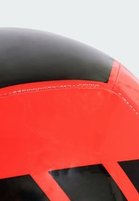 Pallone da calcio rosso e nero con superficie lucida, caratterizzato da una forma curva e cuciture lungo i bordi, che presenta audaci motivi geometrici.