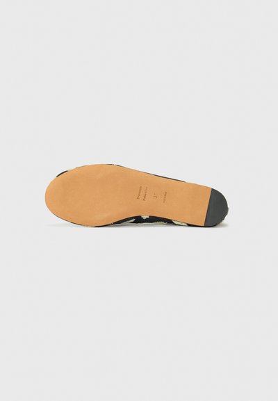 Parte superior de zapato con patrón floral negro, con suela beige plana y suave y tapa de tacón de goma negra. Talla 37 marcada en la plantilla interior.