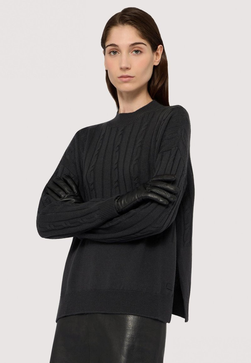 Maglione lavorato a maglia grigio scuro con motivo a trecce, scollo rotondo e vestibilità ampia. Abbinato a guanti in pelle nera e una gonna nera liscia.