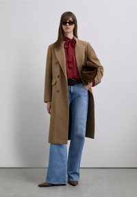 Brown wool overcoat, red blouse with bow, light blue flared jeans, and brown pointed flats. Accessories include sunglasses and a brown bag.