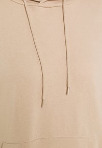 Sudadera beige con un acabado texturizado, cordones y un bolsillo frontal. Presenta un corte relajado y una tela suave.