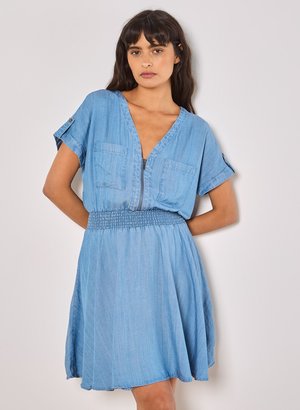 Abito in denim azzurro chiaro con maniche corte, scollatura a V, due tasche frontali, vita arricciata e gonna fluida. Texture morbida, design informale.