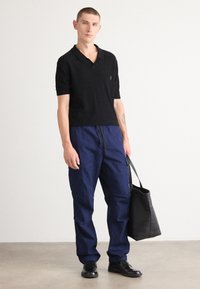 Black knit polo shirt with short sleeves and a subtle logo. Navy blue cargo pants with drawstring waist and side pockets. Black tote bag.