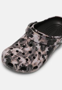 Sabot noir et blanc tie-dye sans lacets avec des trous de ventilation et une bride de talon mobile sur un fond uni.