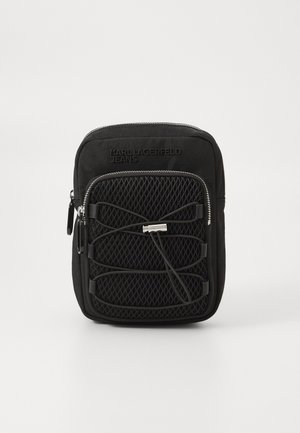 Bolsa transversal preta com frente em malha texturizada, fecho de zip, e design de corda elástica ajustável. Feita de tecido durável.