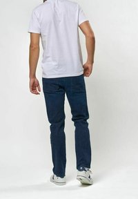 Vit bomullströja med rund halsringning, matchad med mörkblå jeans i denim, försedd med två bakfickor och bärs med vita sneakers.