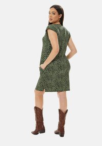 Green leopard print dress with short sleeves, hip pockets, and a knee-length cut, paired with brown cowboy boots.