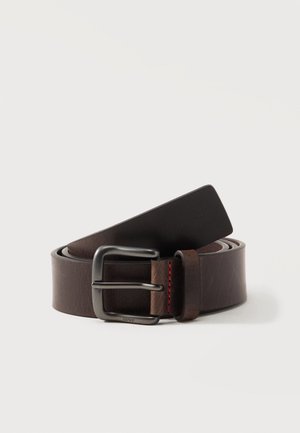 Ceinture en cuir brun foncé avec boucle en métal noir et petit détail de surpiqûres rouges, enroulée sur un fond clair.