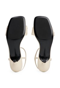 Sandales à talons hauts beiges avec des détails de bride tissée, semelle en cuir lisse, semelle en caoutchouc noir pour une meilleure adhérence, et un design à bout arrondi.