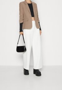 Beige skräddarsydd kavaj, svart kort topp, vita vida byxor, svart lackerad crossbody-väska, kraftiga svarta platåstövlar.