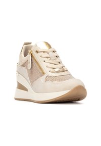 Zapatilla beige con suela de cuña, que presenta materiales de ante y malla, detalle de cremallera dorada y rhinestones decorativos.