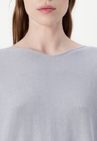 Grå strikket topp med en vid rund halslinning og en myk, teksturert overflate. Stoffet har en subtil glans som gir visuell interesse.