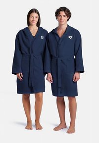 Accappatoi in cotone blu navy con maniche lunghe, cintura e tasche a toppa. Presentano un logo sul petto e un motivo a tinta unita con texture.