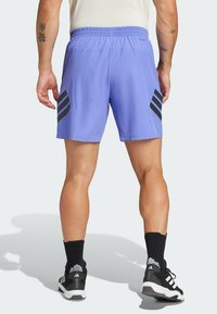 Pantalones cortos deportivos morados con acentos de tres rayas negras, cintura elástica y tejido ligero, usados con calcetines negros y zapatillas.