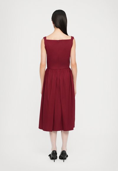 Burgundy sleeveless dress with a square neckline, cinched waist, and pleated skirt, made of smooth fabric. Back features a zip closure.