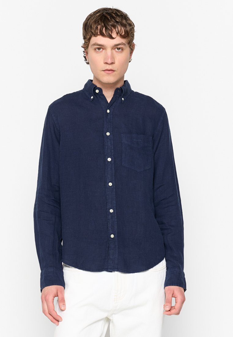 Camisa de botones azul marina en una tela ligera, con un bolsillo en el pecho, dobladillo redondeado y botones blancos. Mangas largas con puños de botón.