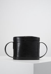 Pyöreä musta keinonahkabag, jossa on teksturoitu krokotiilikuosi, ja siinä on kaksi pyöreää kahvaa sekä kansi.