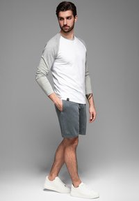 Bílá a šedá košile s dlouhým rukávem v kombinaci se šedými šortkami. Šortky mají kapsy a štítek s logem. Model má na sobě bílé tenisky.