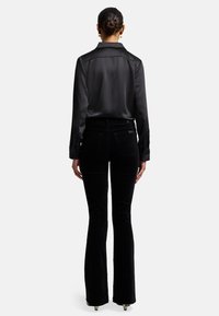 Chemise noire en satin à manches longues avec un col, associée à un pantalon en velours côtelé noir évasé. Accents de boutons visibles et texture lisse.