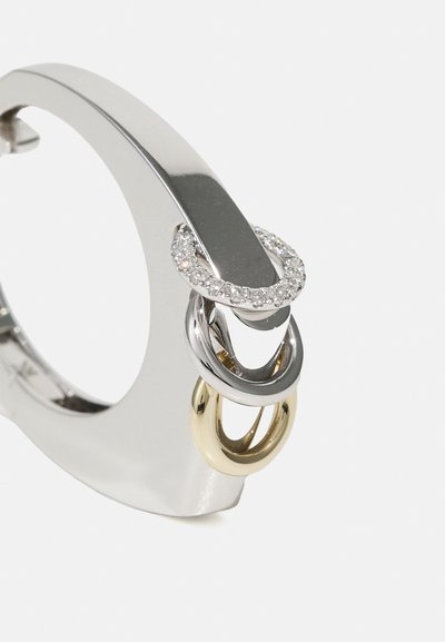 Metāla gredzens ar pulētu sudraba apdari, kam ir trīs savijušies riņķi: viens zelta, viens sudraba un viens, kas rotāts ar mazām caurspīdīgām akmens daļiņām.