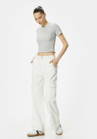Grå tekstureret crop top med korte ærmer, parret med hvide brede cargo bukser med sidelommer og knaplukning.