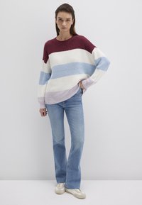 Strickpullover mit horizontalen Streifen in Burgunder, Hellblau, Weiß und Lavendel; kombiniert mit mittelblauen Schlagjeans und beigen Schuhen.
